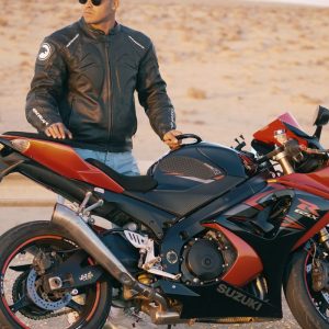 Buneri.es | Bomber, motera o café racer: ¿qué estilo de chaqueta de cuero te queda mejor? Hombre con chaqueta de cuero y gorra posando junto a una moto deportiva en una carretera desértica