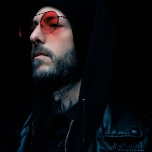 Buneri.es | Chaqueta de Cuero Sobre una Sudadera con Capucha: Cómo Lograr que el Streetwear Funcione Retrato melancólico de un hombre con chaqueta de cuero negra y gafas de tono rojo sobre fondo oscuro