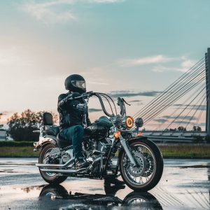 Buneri.es | ¿Se puede llevar una chaqueta de cuero bajo la lluvia? Motociclista con equipo de cuero en una carretera mojada con un puente al fondo al atardecer