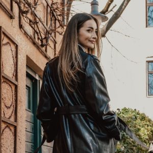 Mujer elegante con un abrigo largo de cuero negro caminando por una calle llena de grafitis