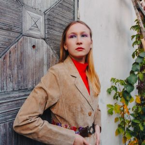 Mujer con chaqueta de ante color tostado apoyada en una vieja puerta desgastada bajo la luz de otono