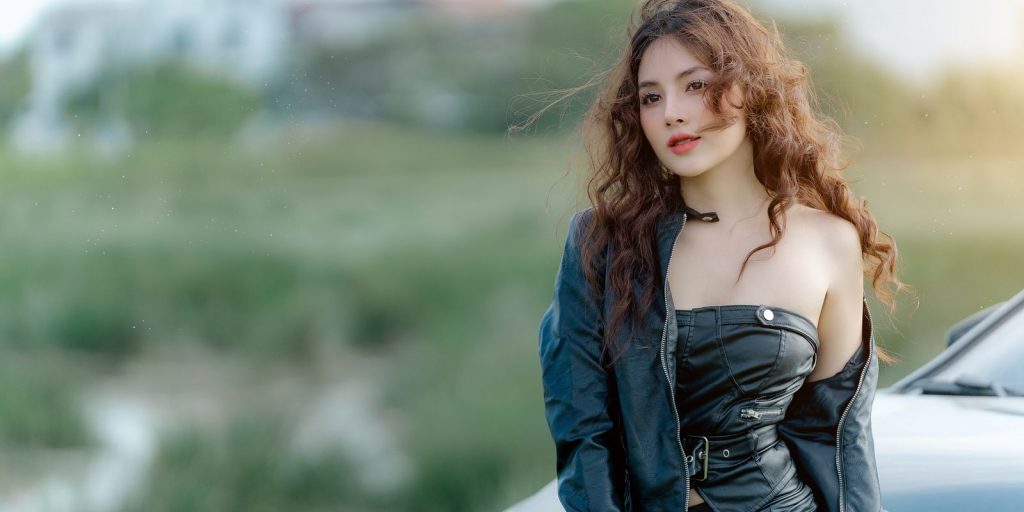 Mujer joven con chaqueta de piel posando con seguridad al aire libre junto a un coche
