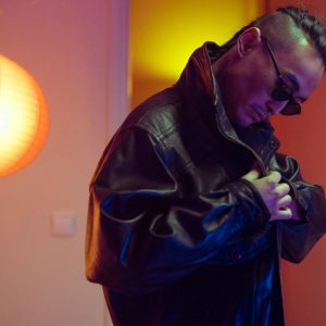 Buneri.es | ¿Las chaquetas de piel se estiran o encogen? La guía del amoldado Hombre elegante con chaqueta de piel negra ajustándose el cuello en un ambiente interior cálido