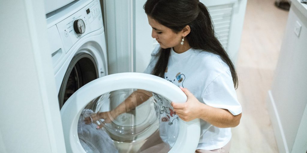 Primer plano de unas manos cargando ropa en una lavadora de carga frontal