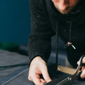 Buneri.es | Reparar una chaqueta de cuero: rotos, arañazos y cremallera Serious male tailor with scissors cutting circle out of leather material while standing at workbench in atelier